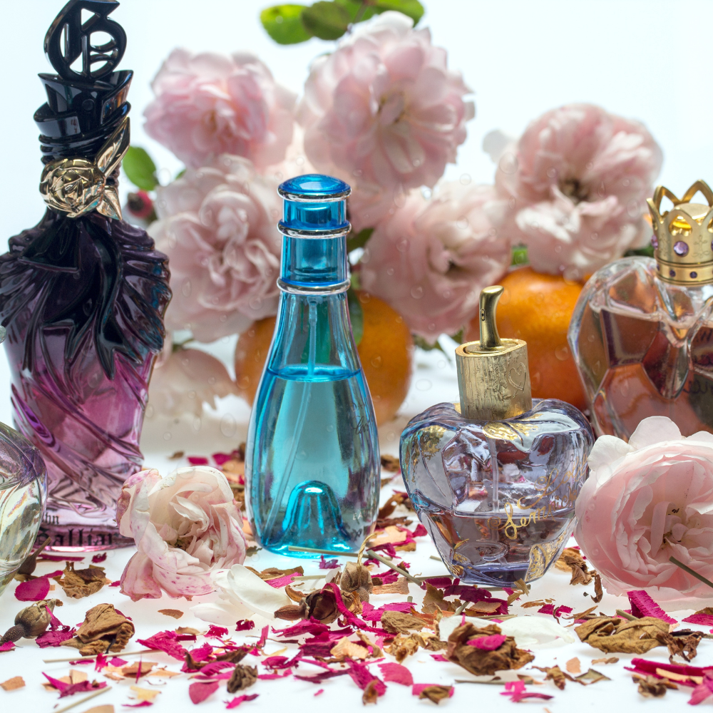 Assorted luxury perfume bottles surrounded by pink flowers, dried petals, and oranges